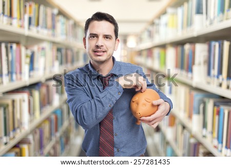 Man wearing a blue shirt and red tie. He is holding a piggy bank. Over library background