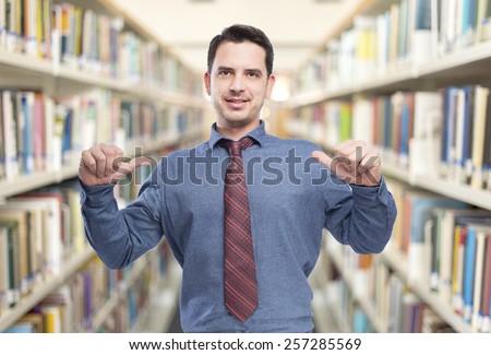 Man wearing a blue shirt and red tie. He is pointing to himself. Over library background