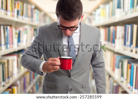 Business man with grey suit. He is blowing into a red cup. Over library background