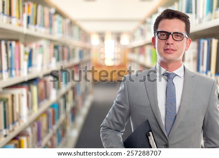 Business man with grey suit. He is holding a black folder. Over library background