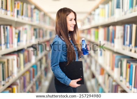Trendy young woman holding a black folder and blue plastic bottle. Over library background