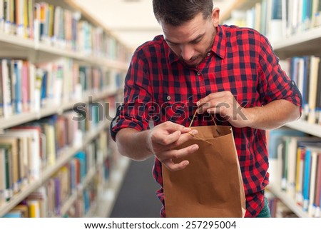 Man with red squares shirt. He is looking surprised inside a brown paper shopping bag. Over library background