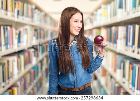 Trendy young woman holding a red apple and smiling. Over library background