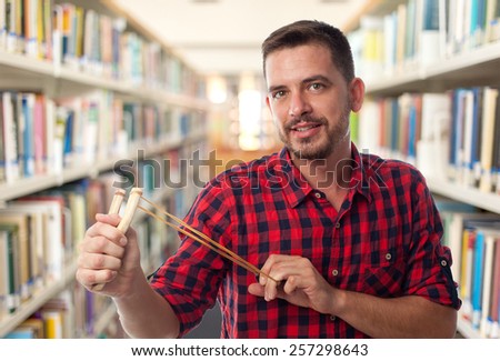 Man with red squares shirt. He is using a slingshot. Over library background