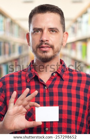 Man with red squares shirt. He is holding a white card. Over library background