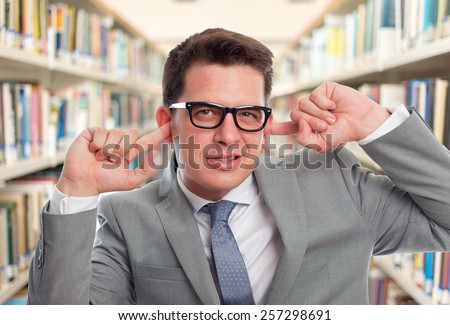 Business man with grey suit. He looks upset because of the noise. Over library background