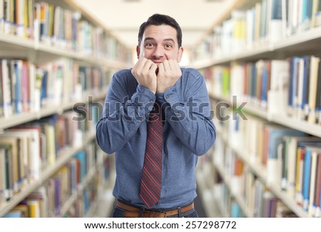 Man wearing a blue shirt and red tie. He is looking afraid. Over library background