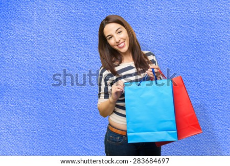 Smiling woman holding red and blue shopping bags. Over blue background