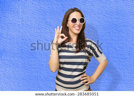 Woman with white sunglasses doing the ok gesture. Over blue background