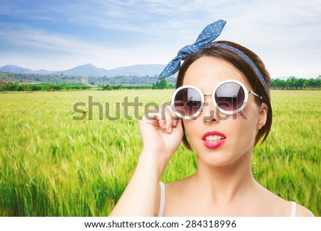 Pin up look woman with white sunglasses. Over meadow background