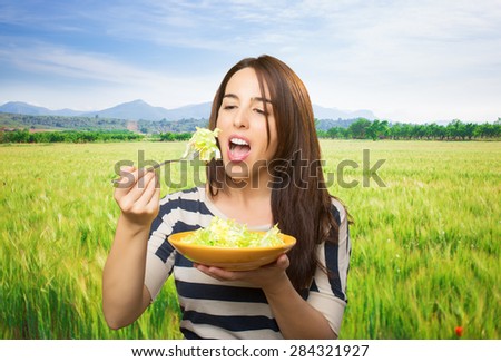 Woman eating a green salad. Over meadow background