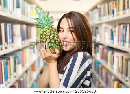 Smiling woman holding a pineapple. Over library background