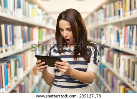Surprised woman using a tablet. Over library background