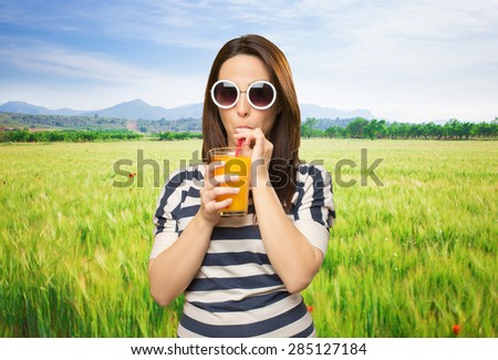 Woman with white sunglasses drinking a juice. Over meadow background