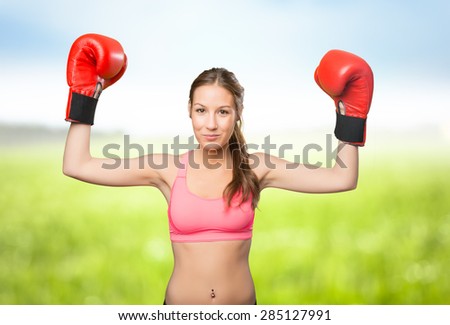 Young woman wearing gym clothes. She looks serious with her boxing gloves. Over nature background