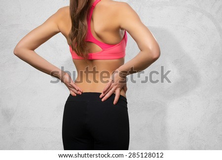 Young woman wearing a gym clothes. She has a back ache. Over concrete background