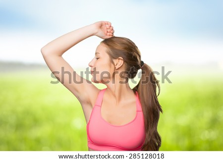 Young woman wearing a gym clothes. She is kissing her biceps. Over nature background