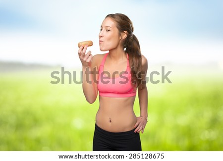 Young woman wearing gym clothes. She is eating a donut. Over nature background