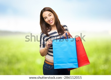 Smiling woman holding red and blue shopping bags. Over nature bokeh background