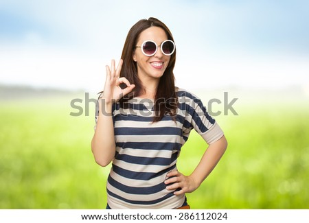 Woman with white sunglasses doing the ok gesture. Over nature bokeh background
