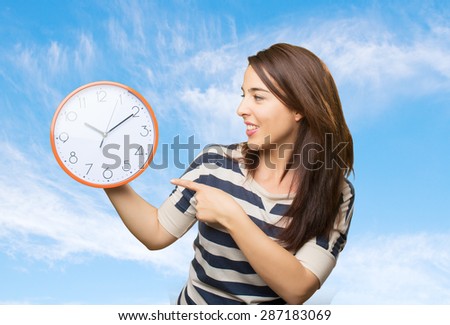 Woman pointing with her finger to a clock. Over clouds background