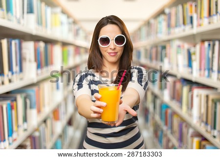Beautiful woman offering a orange juice. Over library background