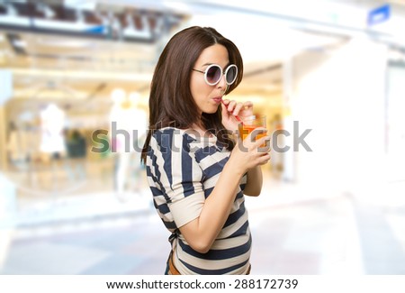 Woman with white sunglasses drinking a juice. Over shopping center background