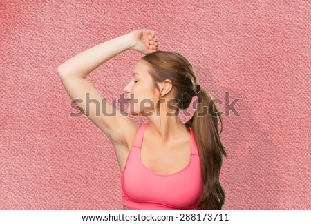 Young woman wearing a gym clothes. She is kissing her biceps. Over red background