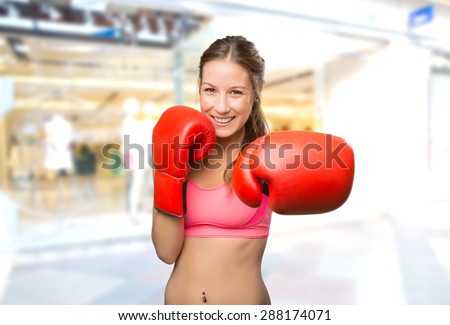 Young woman wearing gym clothes. She has boxing gloves. Over shopping center background