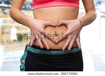 Young woman belly close up with a measurement scale. Over shopping center background