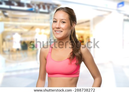 Young woman wearing gym clothes. She is smiling. Over shopping center background