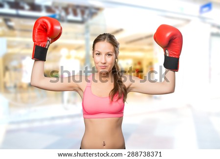 Young woman wearing gym clothes. She looks serious with her boxing gloves. Over shopping center background