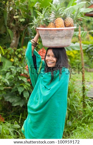 South-east asian woman carrying a basket of pineapples on her head