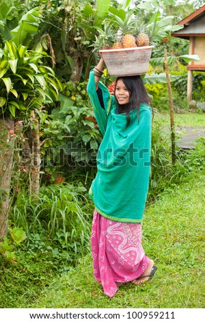 South-east asian woman carrying a basket of pineapples on her head