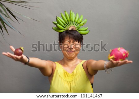 Woman making face with holding fresh fruit and bananas on head