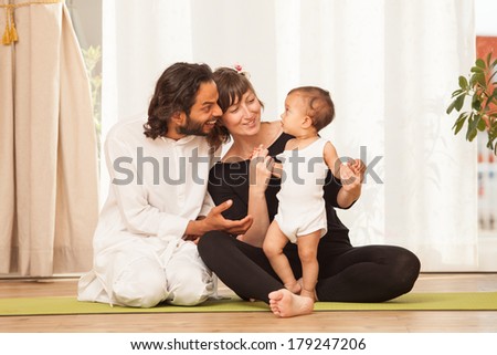 Happy yoga multiethnic couple with a child posing and practicing yoga, in an yoga studio environment full of light.