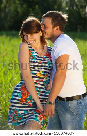 Young couple are on meadow on forest background. Girl and guy love each other. They are very funny. The guy has a watch on his arm.
