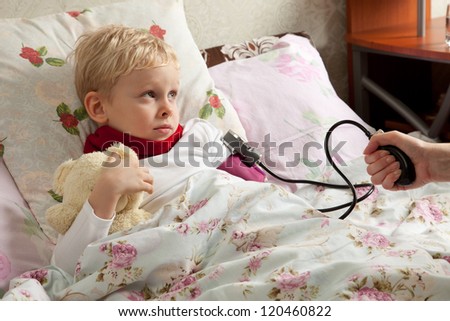Sick boy is laying in bed with his teddy bear. His blood pressure is measured tonometer.