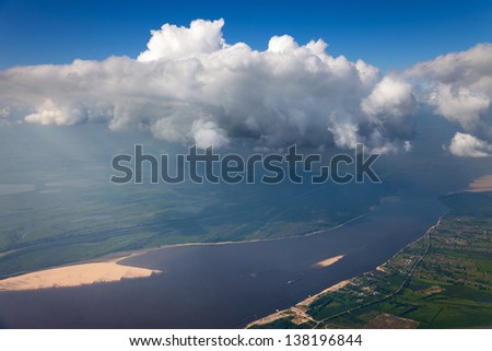 Aerial view of great stormy clouds which hang over the great river during a flight in summer.