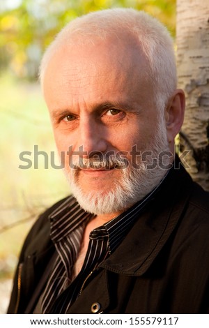 Elderly man with gray beard for a walk in the forest at the beginning autumn