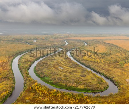 Aerial view of forest river in cloudy autumn day. Leafs of trees are painted in different bright colors.