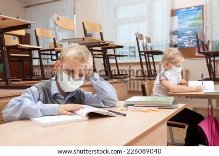 School children in medical face mask are learning in the half empty classroom during epidemic of flu.