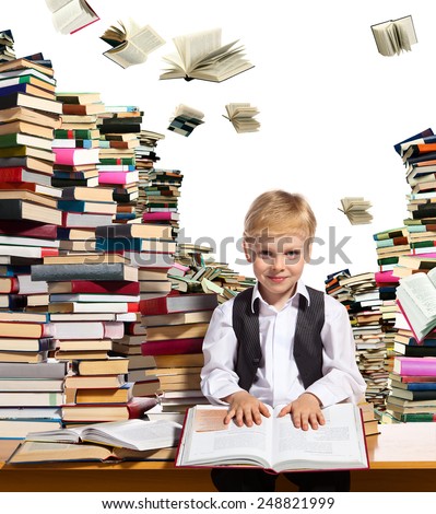 Little boy is reading interesting book. High stacks of books are on the table near him.