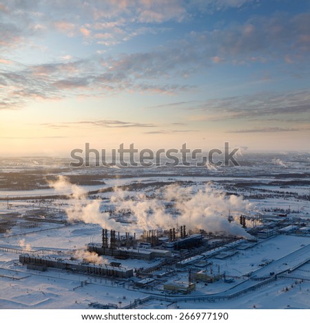 Aerial view of the oil refinery with smoking chimneys in winter against sunset. West Siberia.