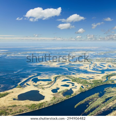 Aerial view over flood-land beside great river during spring. Great plain is divided into many parts by a lot of number of rivers and channels. Water meadows are covered by yellow last year\'s grass.