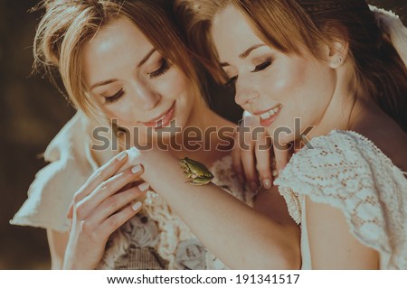 Twin sisters holding in his hand a green frog