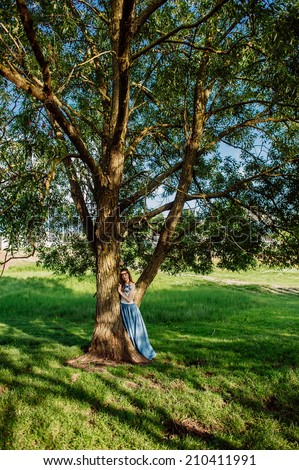 beautiful girl in a long dress standing near a tree