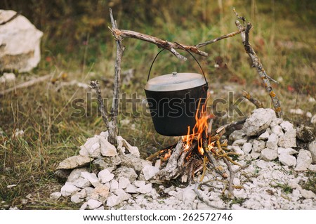The image of a fire in the woods on which is brewed pot