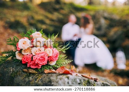 Newly-married couple and wedding bouquet in the foreground. Wedding bouquet with the wedding couple in the background