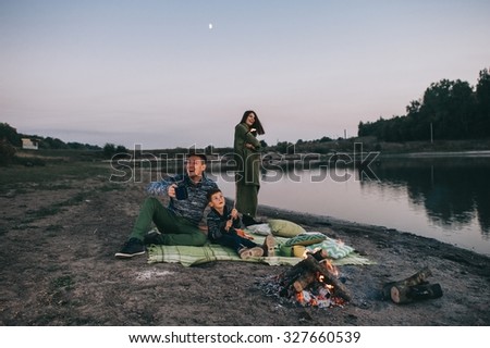 Happy young family sitting around the campfire on the beach at night fall, mother, father, son